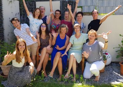 Isabel Ihm, NLP-Premium-Trainerin, sitzt inmitten von lachenden Teilnehmerinnen im Garten